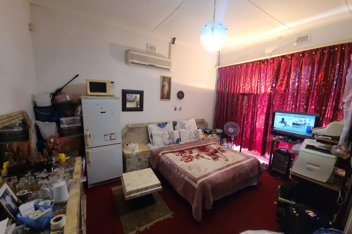 A bedroom featuring a built-in headboard, split-system air conditioning, and ceiling pendant lighting, currently requiring cosmetic updates to the flooring and ceiling finishes.