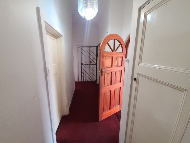 A narrow hallway featuring carpet flooring, a timber panelled door, and a security gate at the end.