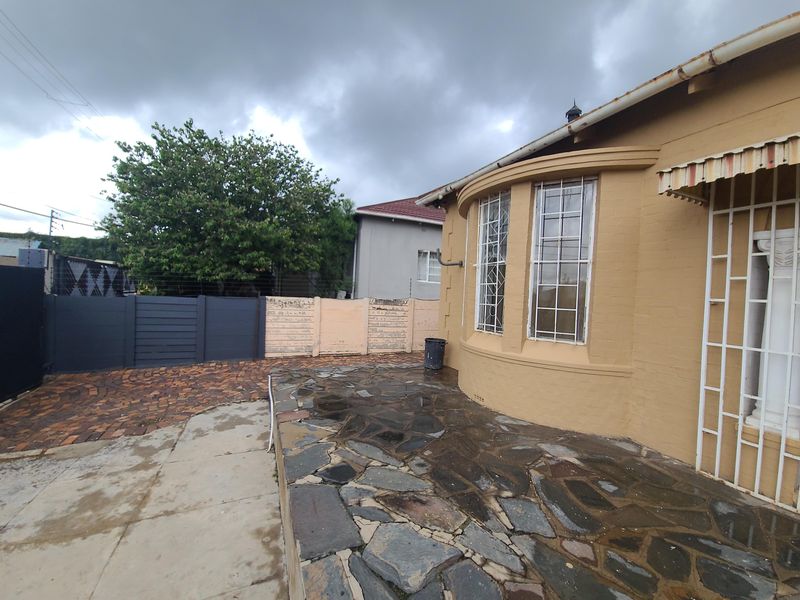 Rear exterior view of the property featuring a stone paved patio, brick driveway, and security bars on the windows.