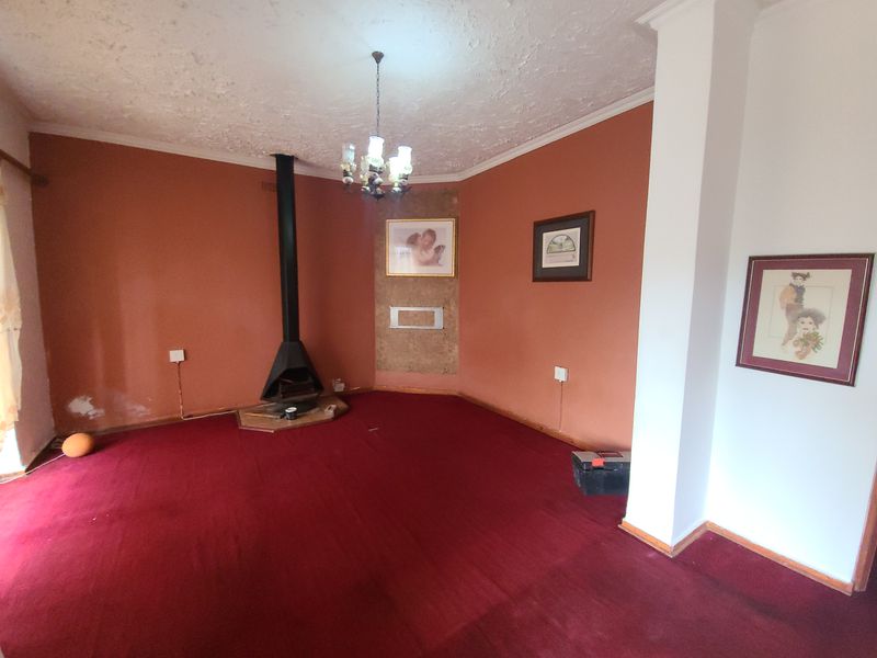 Spacious living room featuring a freestanding fireplace, carpeted flooring, and a central chandelier, offering a blank canvas for renovation and modernization.