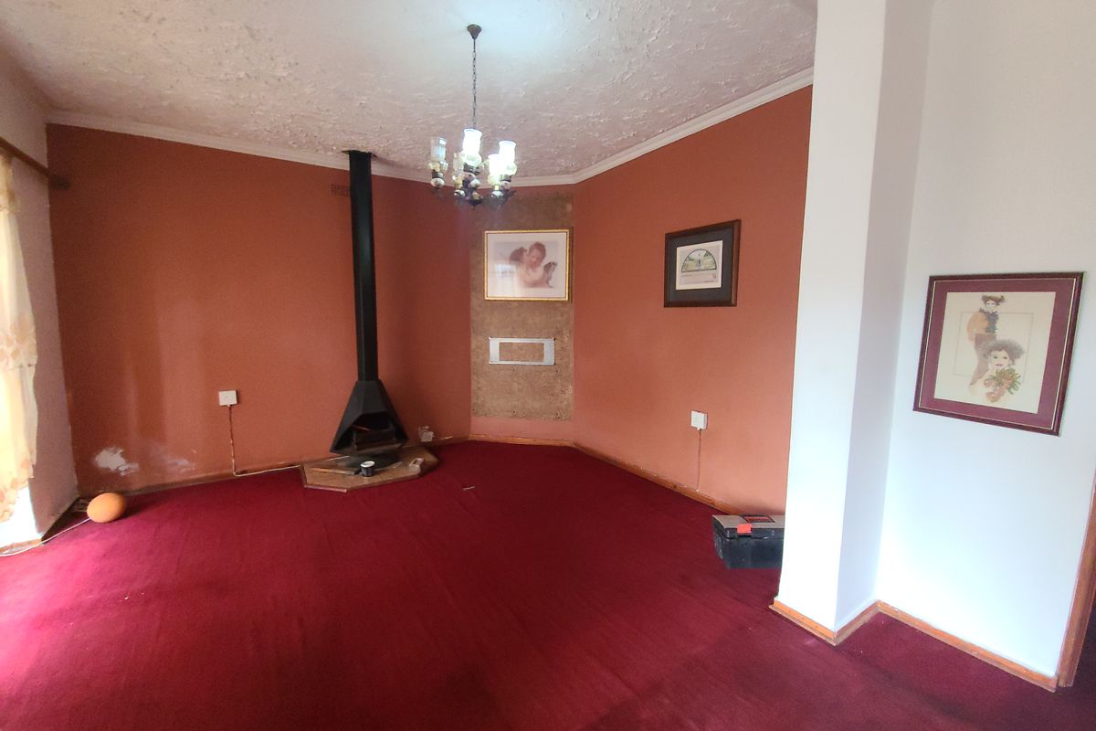 Spacious living room featuring a freestanding fireplace, carpeted flooring, and a central chandelier, offering a blank canvas for renovation and modernization.