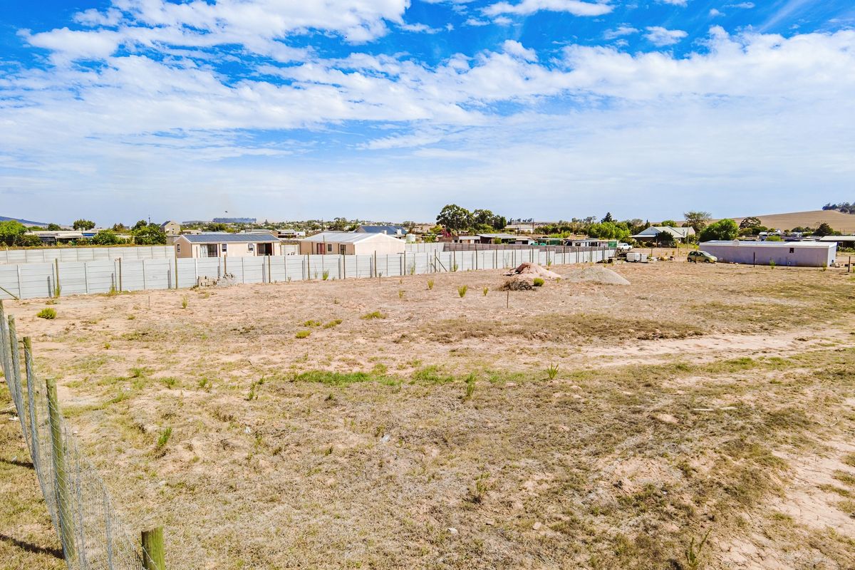 A vacant residential plot featuring a level landscape, enclosed by precast concrete boundary walls and wire mesh fencing in a suburban setting.