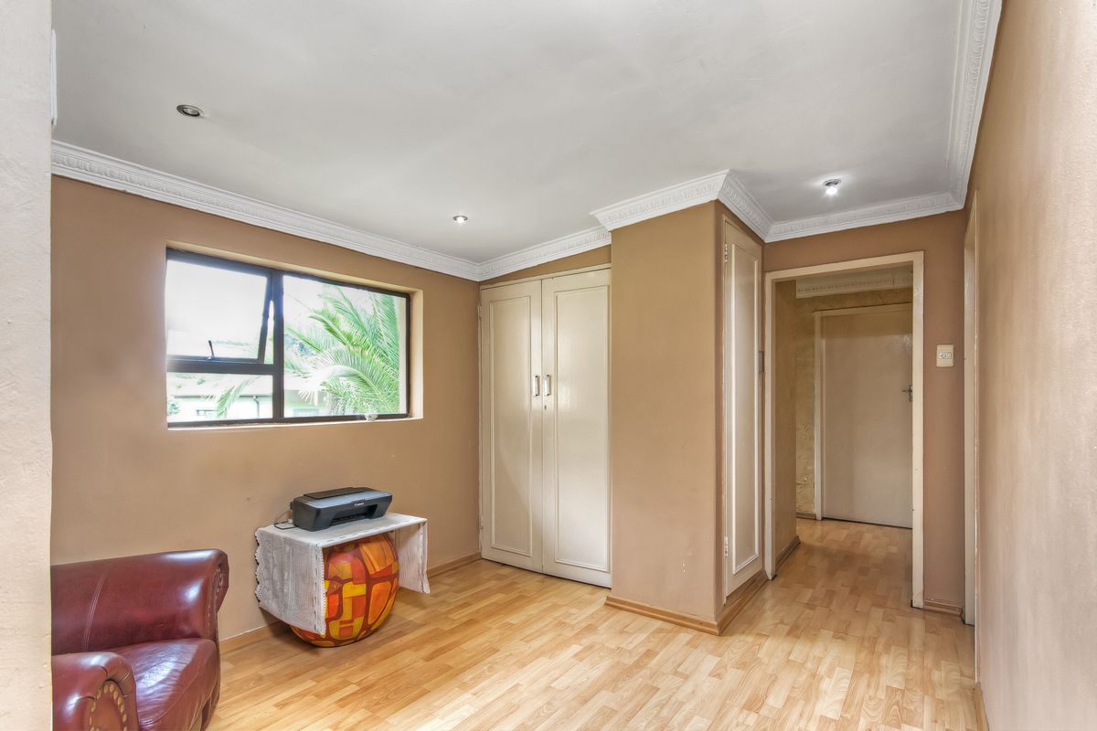 A bedroom featuring built-in cupboards, laminate flooring, and decorative ceiling cornicing, providing a functional and well-lit living space.