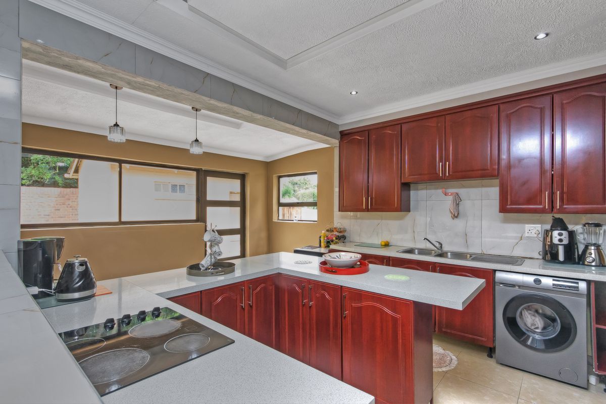 A functional kitchen featuring dark wood cabinetry, stone-look countertops, a built-in electric hob, and an integrated laundry appliance space.