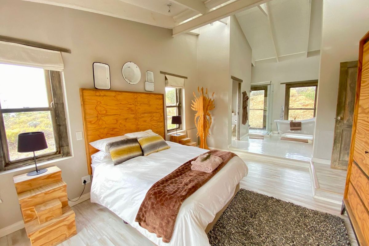 Spacious bedroom featuring vaulted ceilings with exposed beams, integrated en-suite bathroom with a freestanding bathtub, and large windows offering natural light.