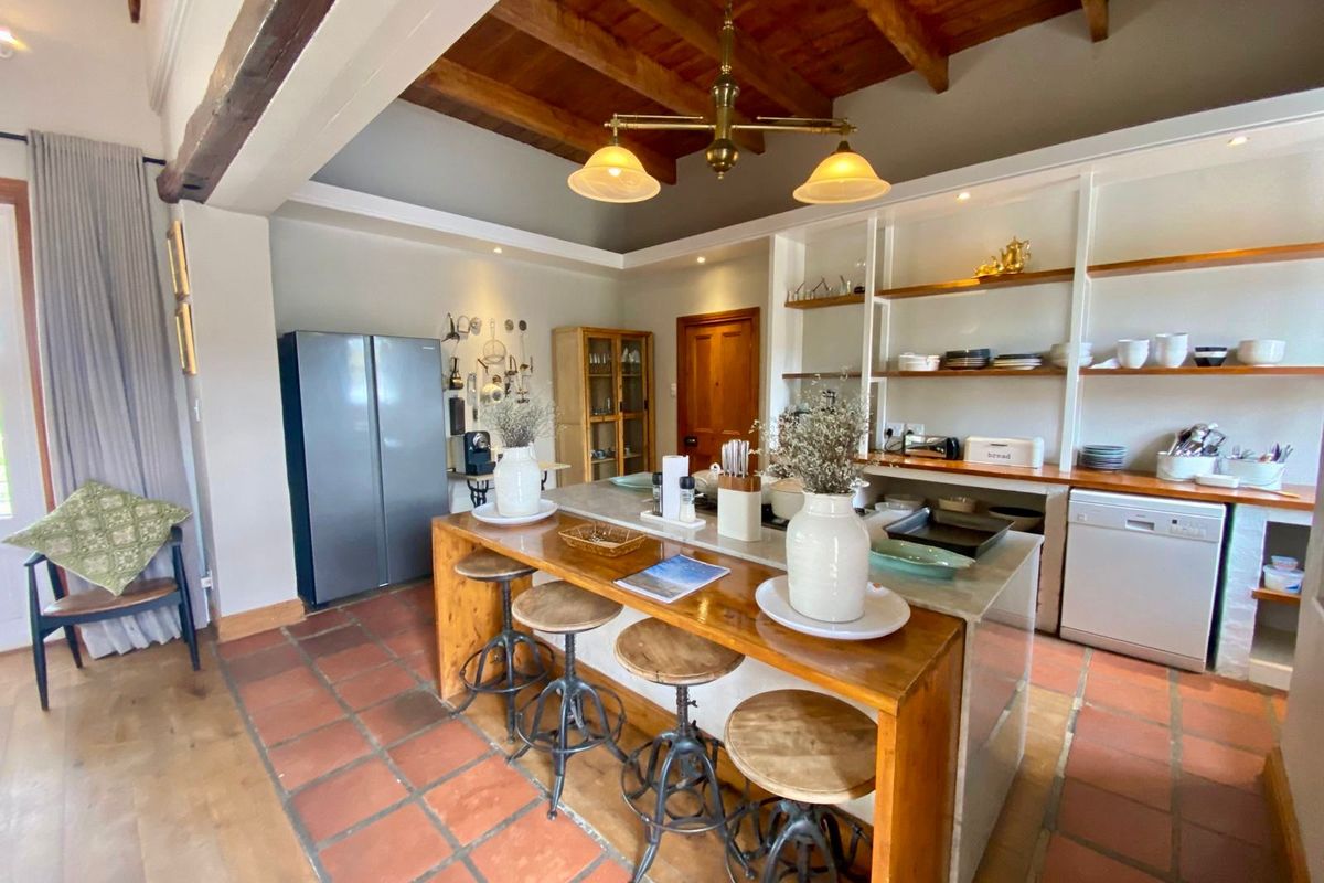Spacious farmhouse kitchen featuring a large central island with breakfast bar, open shelving, exposed timber ceiling beams, and traditional terracotta floor tiles.