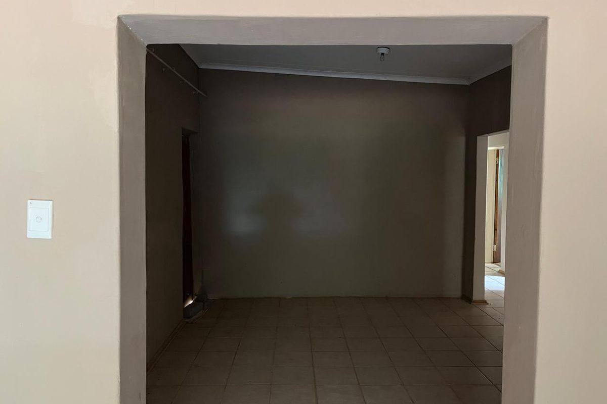 An empty, neutrally painted room featuring tiled flooring and a wide doorway leading to an adjacent space.