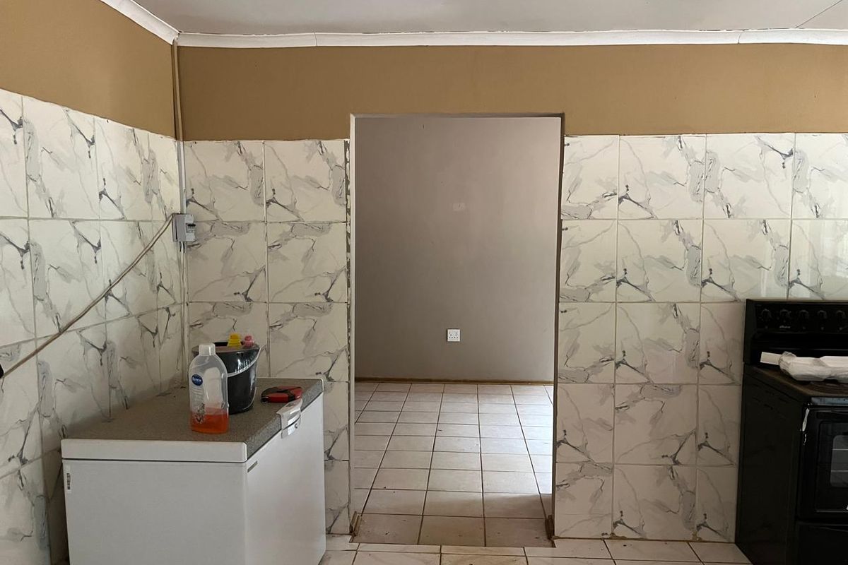A functional kitchen area featuring marble-effect wall tiling, tiled flooring, and a doorway leading to an adjacent room.