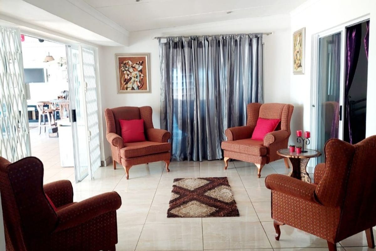 A bright living room featuring large format floor tiles, recessed ceiling lighting, and sliding glass doors leading to an adjacent patio area.