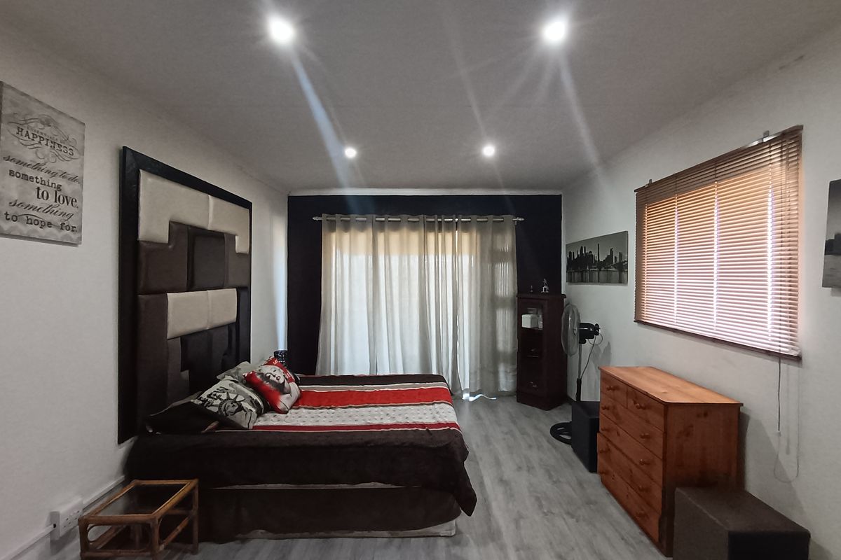 A well-maintained bedroom featuring modern laminate flooring, recessed ceiling downlights, and a large window fitted with wooden venetian blinds.