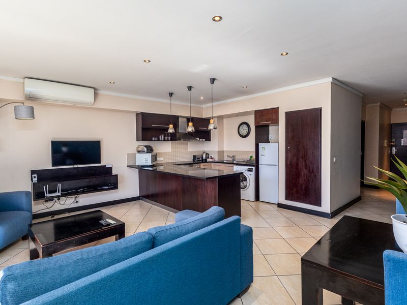 Open-plan living area featuring a modern kitchen with dark wood cabinetry, granite countertops, and tiled flooring, seamlessly integrated with the lounge space.