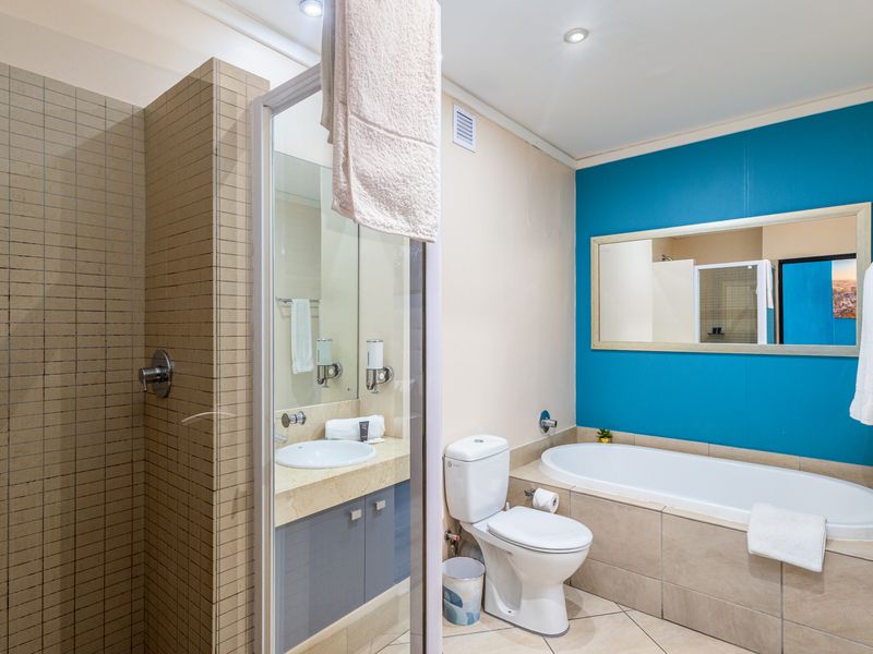 A well-maintained bathroom featuring a separate shower enclosure, built-in vanity with basin, toilet, and a bathtub with a feature wall.