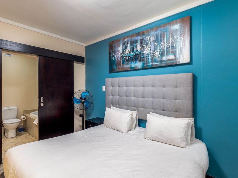A bedroom featuring a bold blue accent wall, a sliding door providing access to an en-suite bathroom, and neutral tiled flooring.