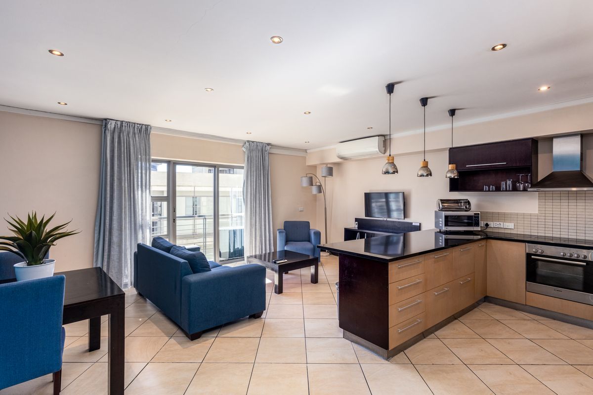 Open-plan living area featuring a modern kitchen with a central island, tiled flooring, and direct access to a balcony through sliding glass doors.