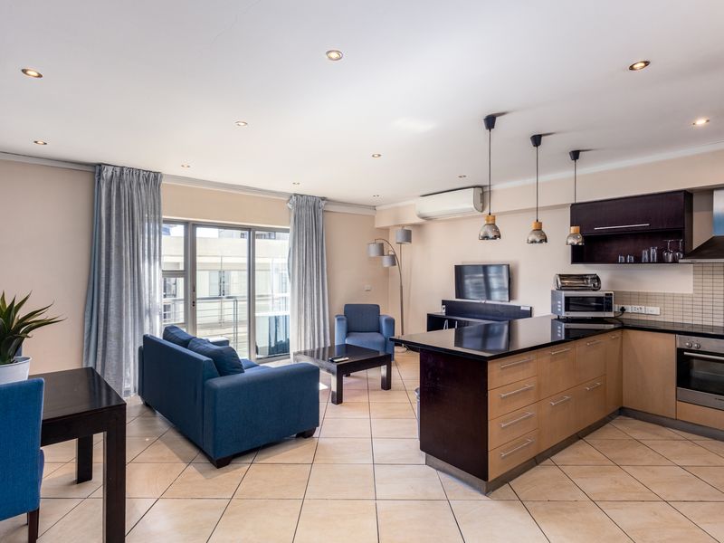 Open-plan living area featuring a modern kitchen with a central island, tiled flooring, and direct access to a balcony through sliding glass doors.
