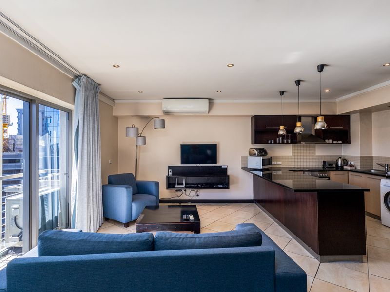 Open-plan living area featuring a modern kitchen with dark cabinetry, granite countertops, integrated appliances, and direct access to a private balcony.
