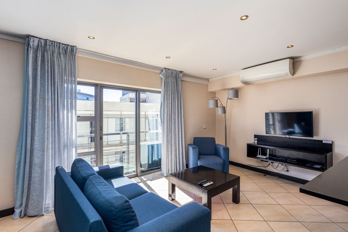 A well-lit living room featuring tiled flooring, a wall-mounted air conditioning unit, and a sliding glass door providing access to the balcony.