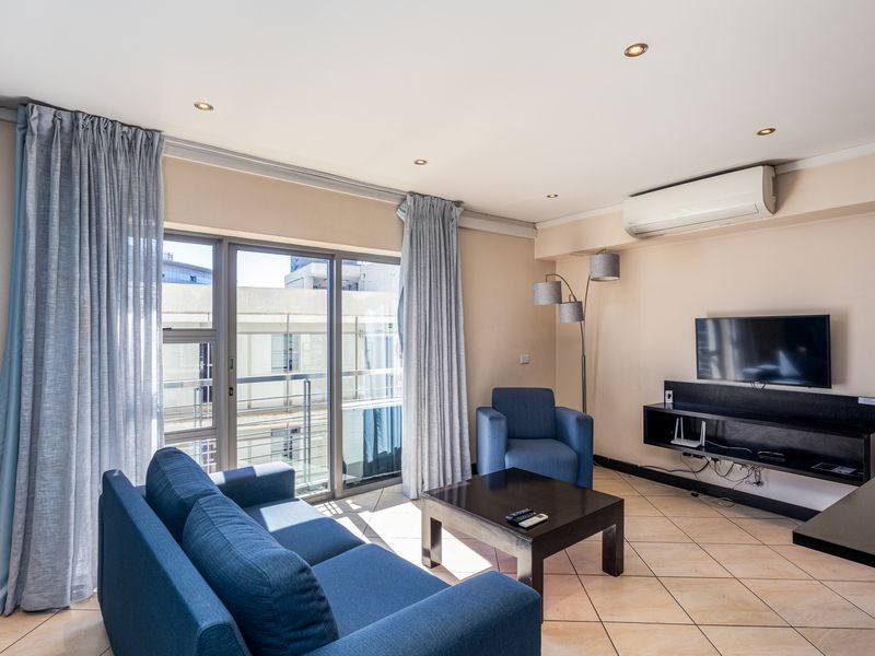 A well-lit living room featuring tiled flooring, a wall-mounted air conditioning unit, and a sliding glass door providing access to the balcony.