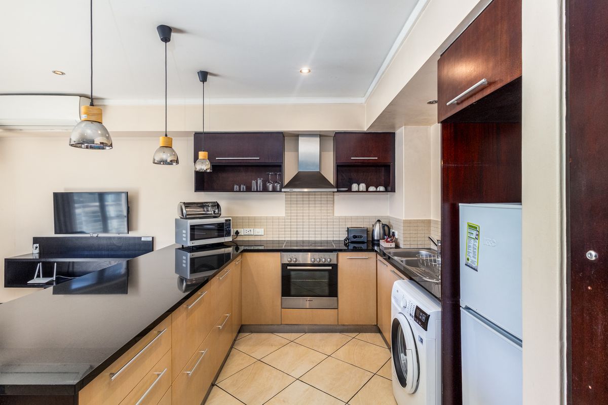 Open-plan kitchen featuring modern cabinetry, granite countertops, integrated appliances, and a breakfast bar, seamlessly flowing into the living area.