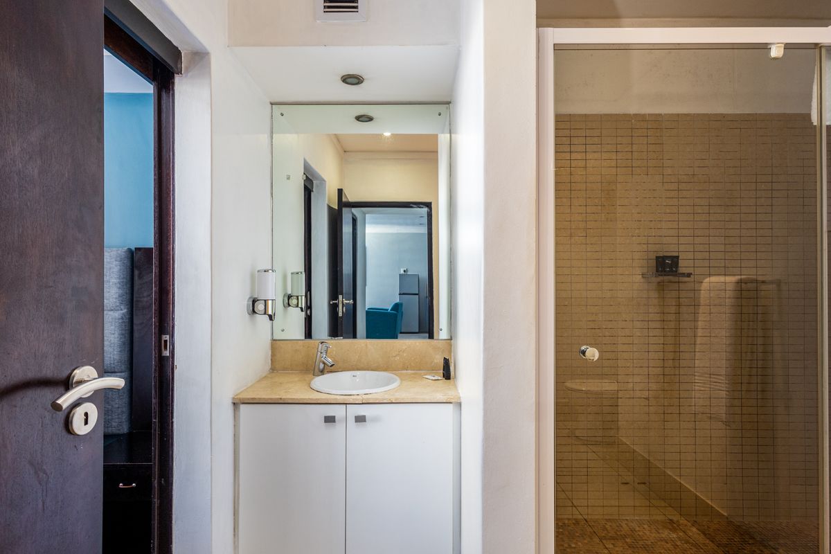 A functional bathroom featuring a vanity with stone countertop, integrated sink, wall mirror, and a separate shower enclosure with tiled walls.