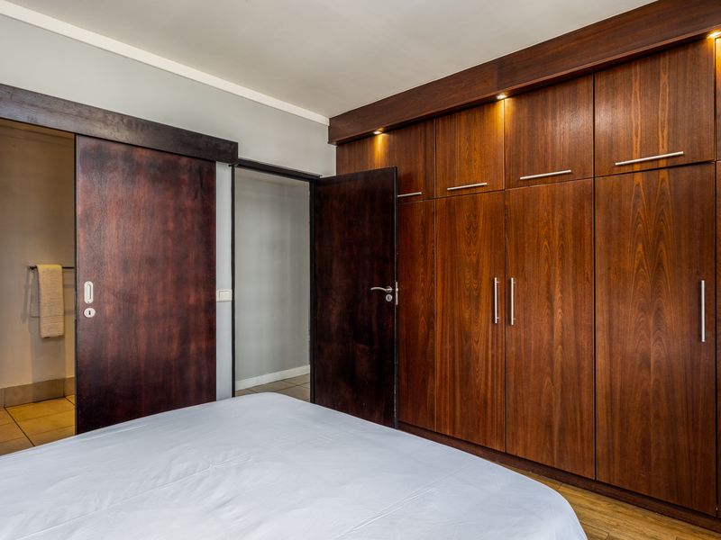 A well-maintained bedroom featuring extensive built-in dark wood cabinetry with integrated lighting and a sliding door leading to an en-suite bathroom.
