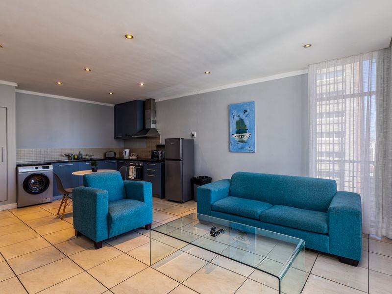 An open-plan living area featuring a modern kitchen with built-in cabinetry, tiled flooring, and recessed lighting, seamlessly integrated with a comfortable lounge space.