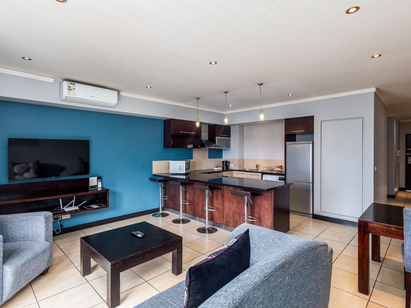 Open-plan living area featuring a modern kitchen with granite countertops, breakfast bar, and tiled flooring, seamlessly integrated with the lounge space.