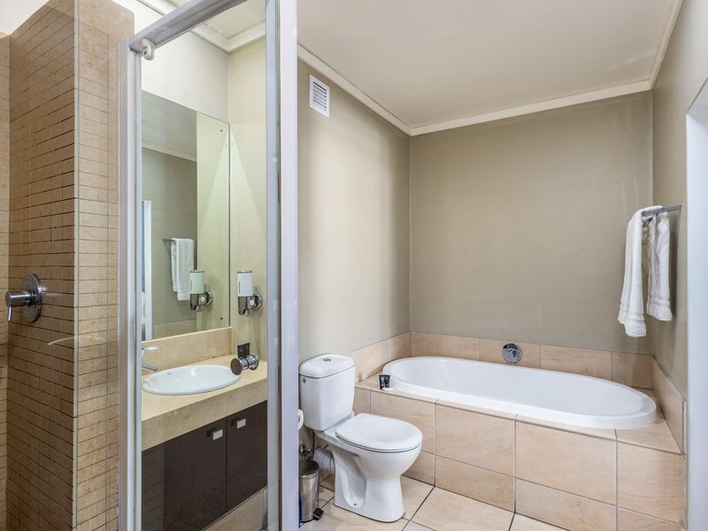 A clean, functional bathroom featuring a built-in bathtub, separate shower enclosure, vanity with integrated sink, and neutral tile finishes.
