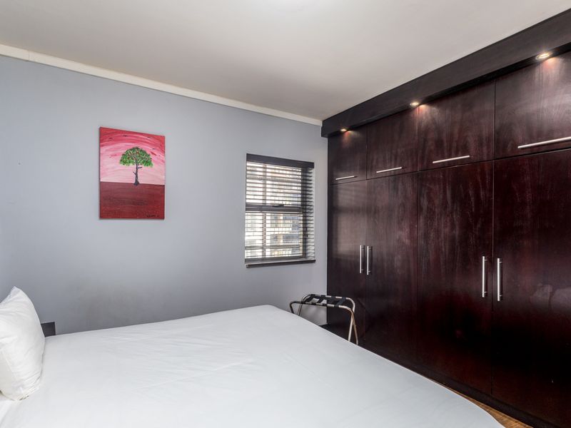 A well-maintained bedroom featuring dark wood built-in cupboards with integrated downlighting and a window fitted with venetian blinds.