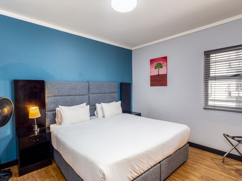 A well-maintained bedroom featuring laminate flooring, a blue accent wall, and venetian blinds, providing a clean and functional living space.