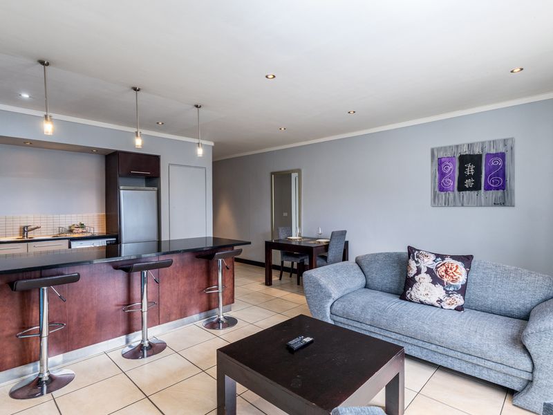 Open-plan living area featuring a modern kitchen with granite countertops, breakfast bar, and tiled flooring throughout the combined lounge and dining space.