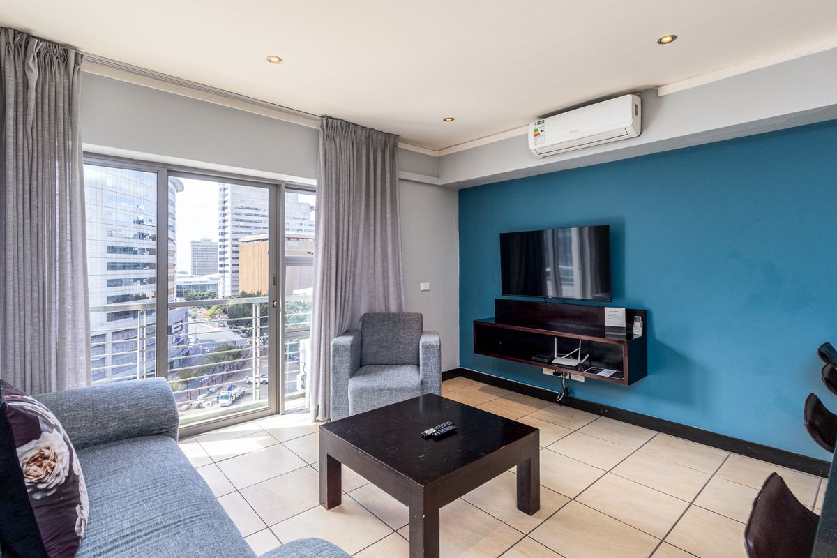 A modern living room featuring tiled floors, a wall-mounted media console, air conditioning, and a sliding glass door leading to a balcony with city views.