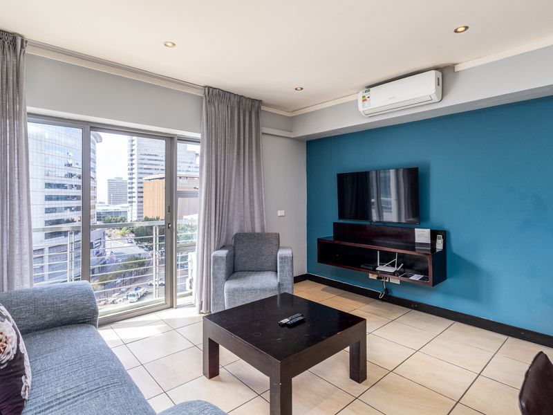 A modern living room featuring tiled floors, a wall-mounted media console, air conditioning, and a sliding glass door leading to a balcony with city views.