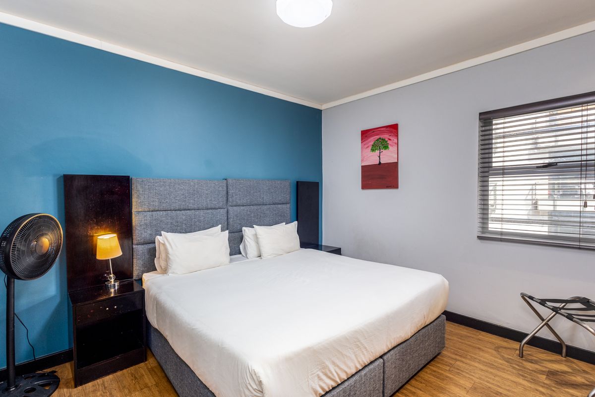 A well-maintained bedroom featuring laminate flooring, a blue accent wall, and venetian blinds, providing a clean and functional living space.