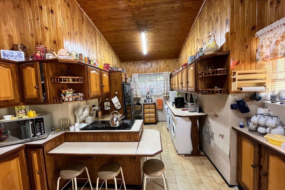 A traditional kitchen featuring extensive wood-paneled walls and ceilings, built-in cabinetry, a central hob, and integrated laundry appliance connections.