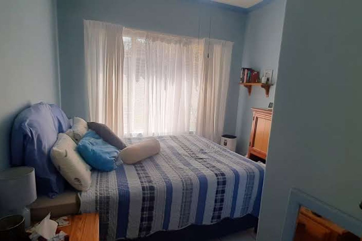 A cozy bedroom featuring a large window with sheer curtains, providing natural light and a comfortable living space.