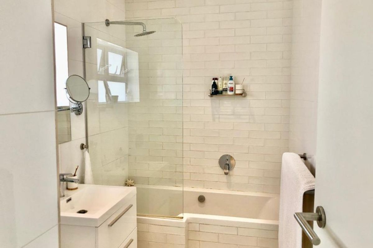 Modern bathroom featuring a built-in bathtub with a glass shower screen, subway tile surround, and a contemporary vanity unit.