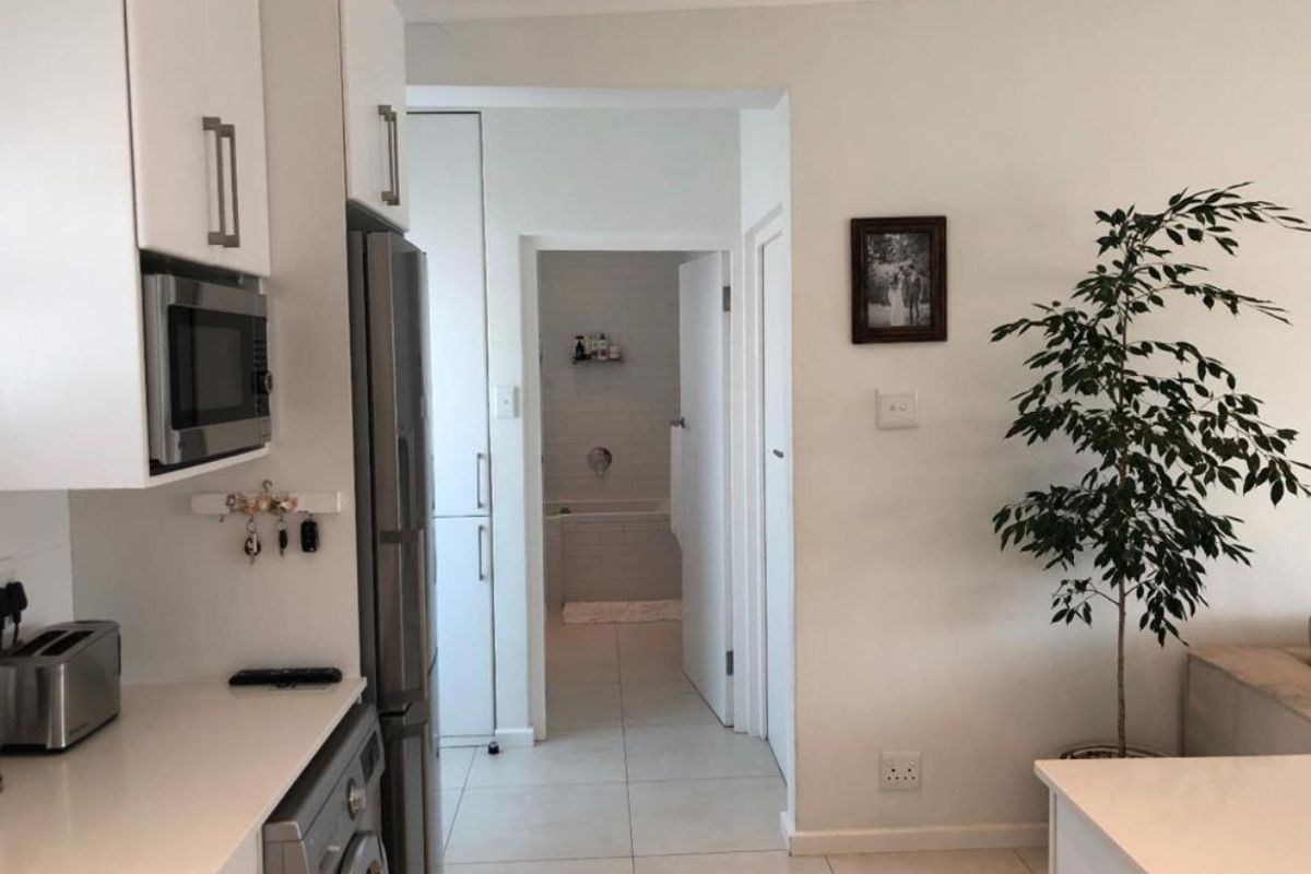 A view from the kitchen area looking towards a bathroom, featuring white cabinetry, tiled flooring, and a built-in microwave.