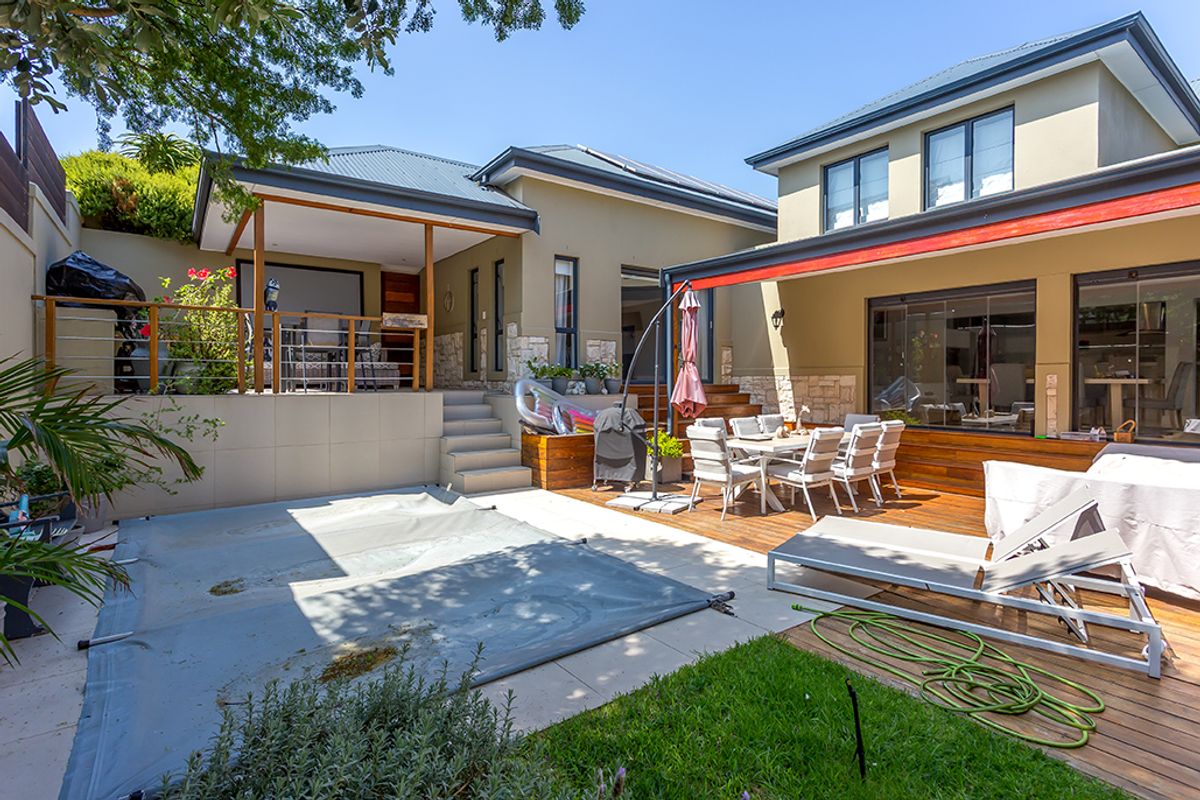 A spacious rear outdoor area featuring a swimming pool with cover, timber decking, a covered patio, and landscaped garden elements.