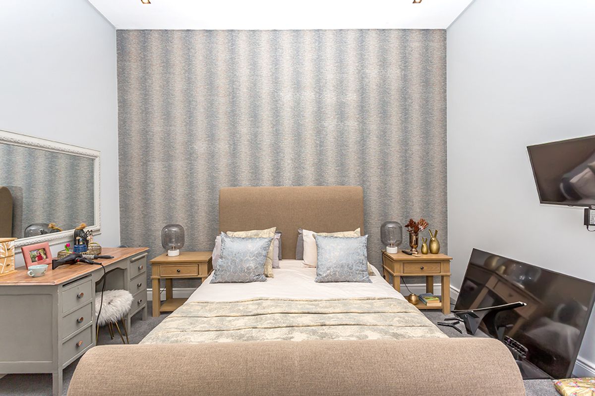 A well-presented bedroom featuring a textured feature wall, neutral carpeting, and recessed ceiling lighting.