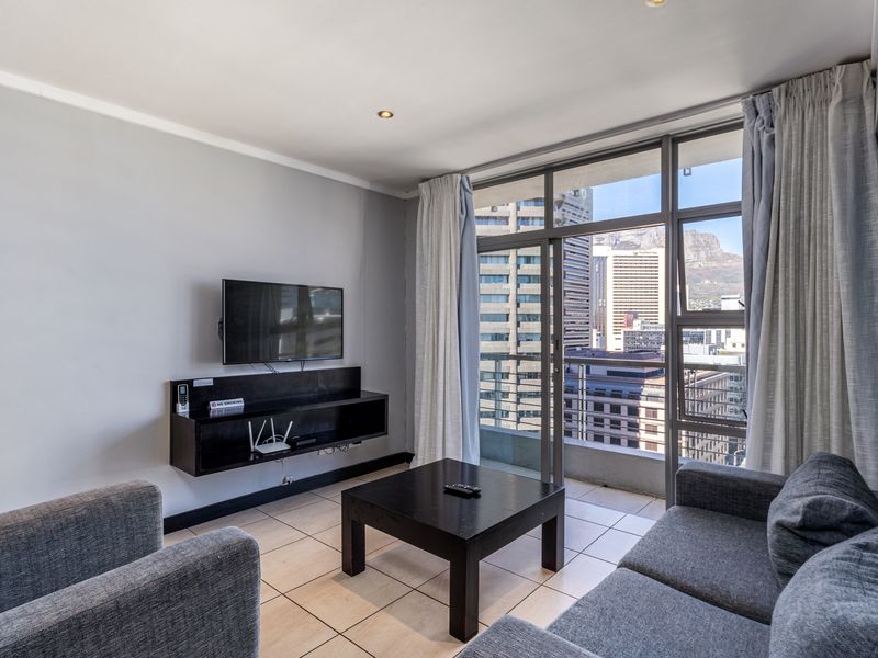 A bright living room featuring tiled floors, a wall-mounted media console, and large sliding glass doors opening to a balcony with city views.
