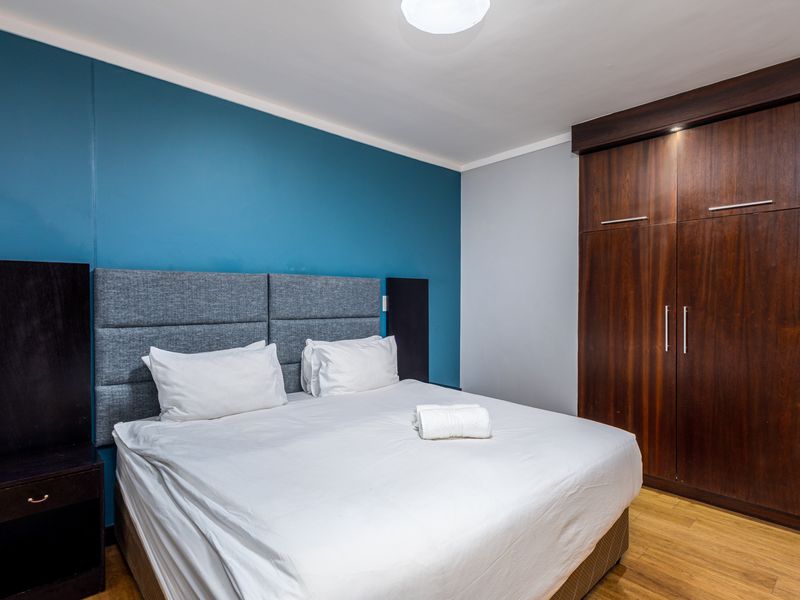 A well-maintained bedroom featuring laminate flooring, a bold blue accent wall, and a large built-in wooden wardrobe.