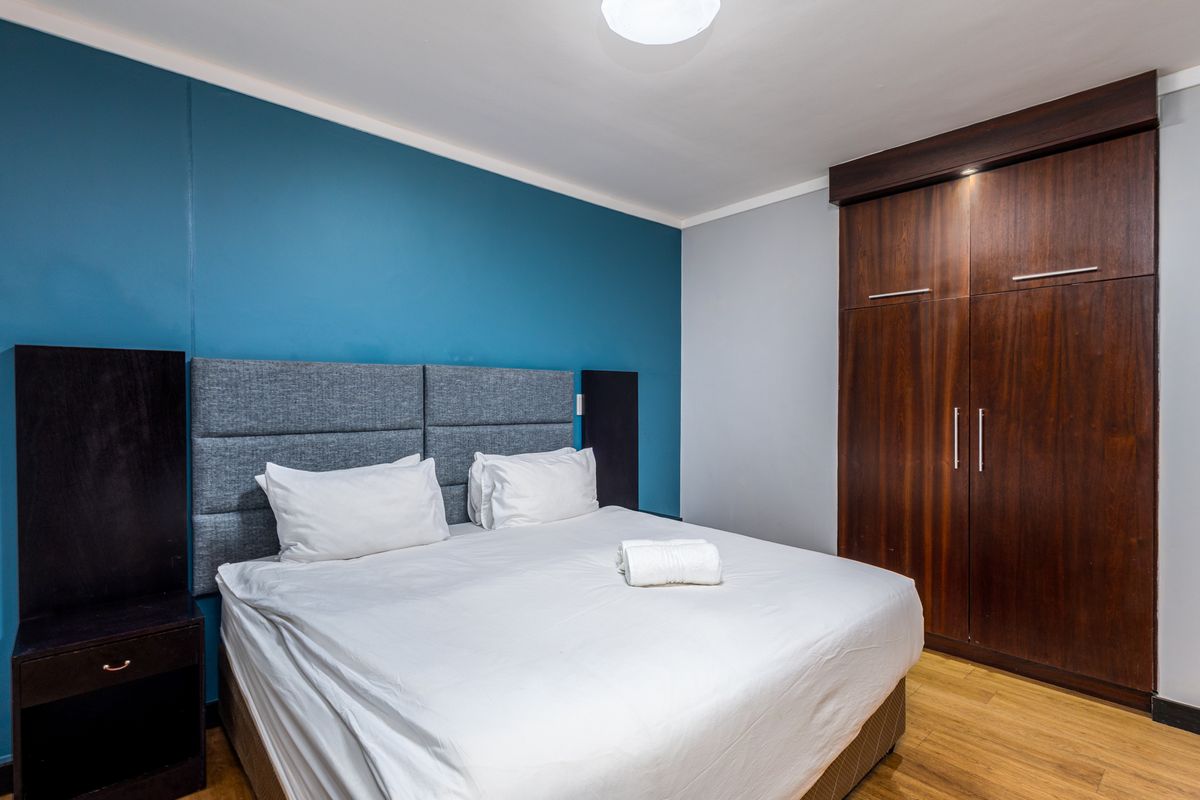 A well-maintained bedroom featuring laminate flooring, a bold blue accent wall, and a large built-in wooden wardrobe.