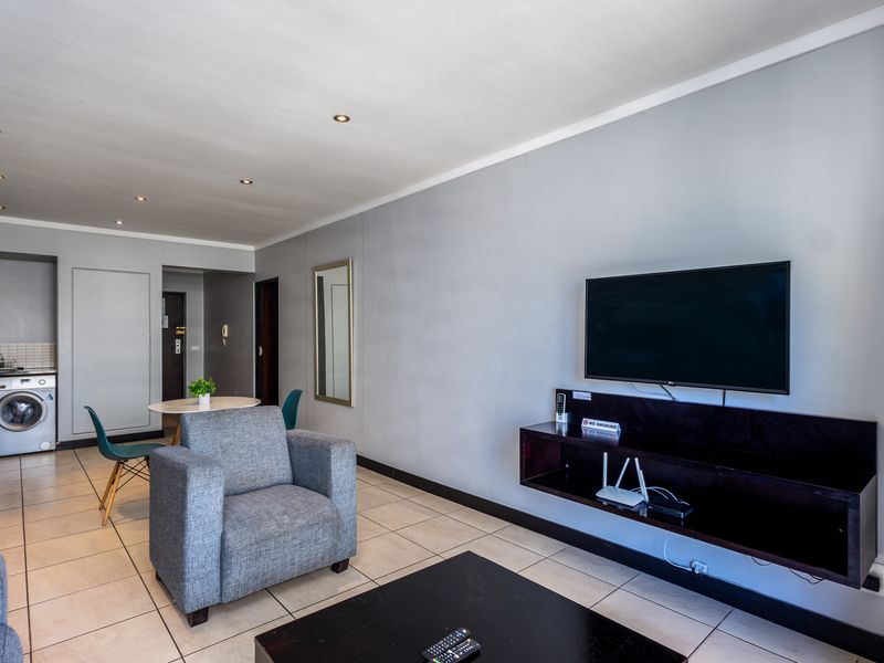 Open-plan living area featuring tiled floors, recessed lighting, and a compact kitchen corner with built-in cabinetry and laundry facilities.
