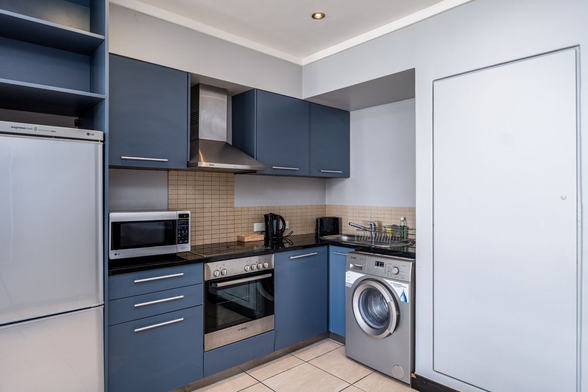 Compact modern kitchen featuring blue cabinetry, integrated stainless steel appliances, tiled backsplash, and tiled flooring.