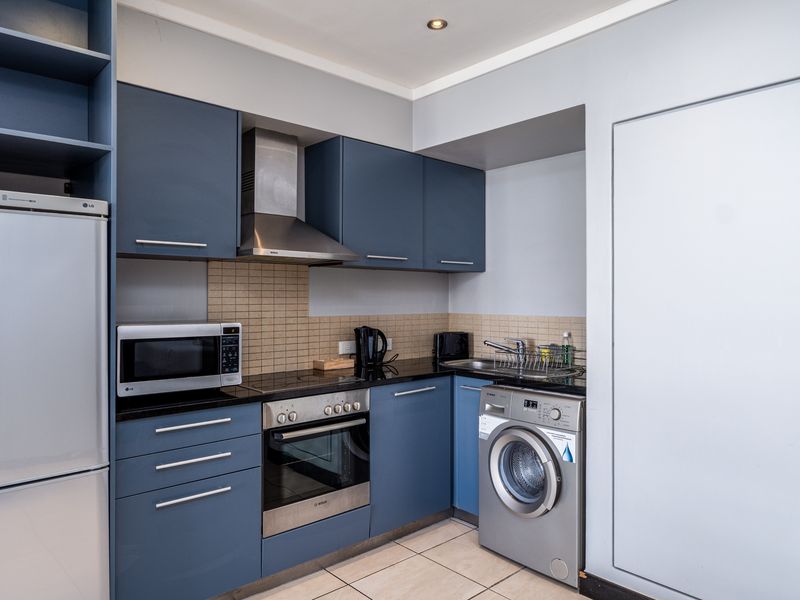 Compact modern kitchen featuring blue cabinetry, integrated stainless steel appliances, tiled backsplash, and tiled flooring.