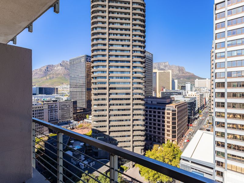An elevated city view from a balcony, showcasing surrounding high-rise buildings and mountain scenery in the background.