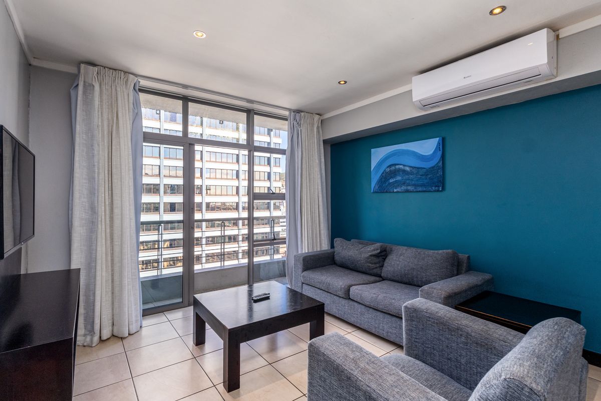 A well-maintained living room featuring tiled floors, a split-system air conditioner, and large sliding glass doors providing natural light and balcony access.