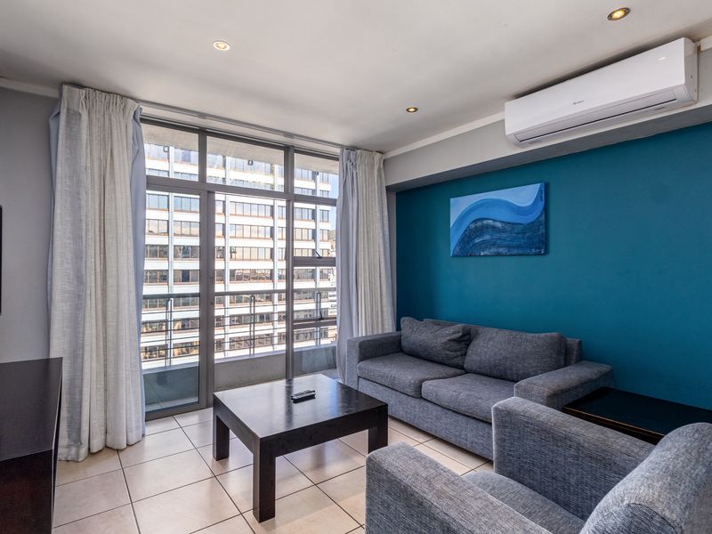 A well-maintained living room featuring tiled floors, a split-system air conditioner, and large sliding glass doors providing natural light and balcony access.