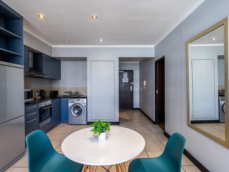 Open-plan kitchen area featuring modern blue cabinetry, integrated appliances, tiled flooring, and recessed lighting, seamlessly connecting to the apartment entrance.